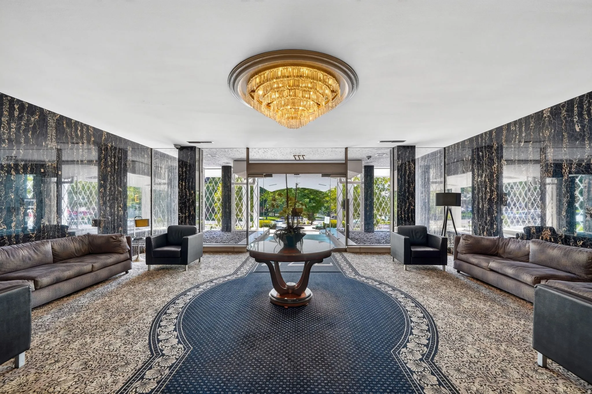 Spacious lobby featuring a large chandelier, dark patterned wallpaper, floor-to-ceiling windows, and a decorative area rug