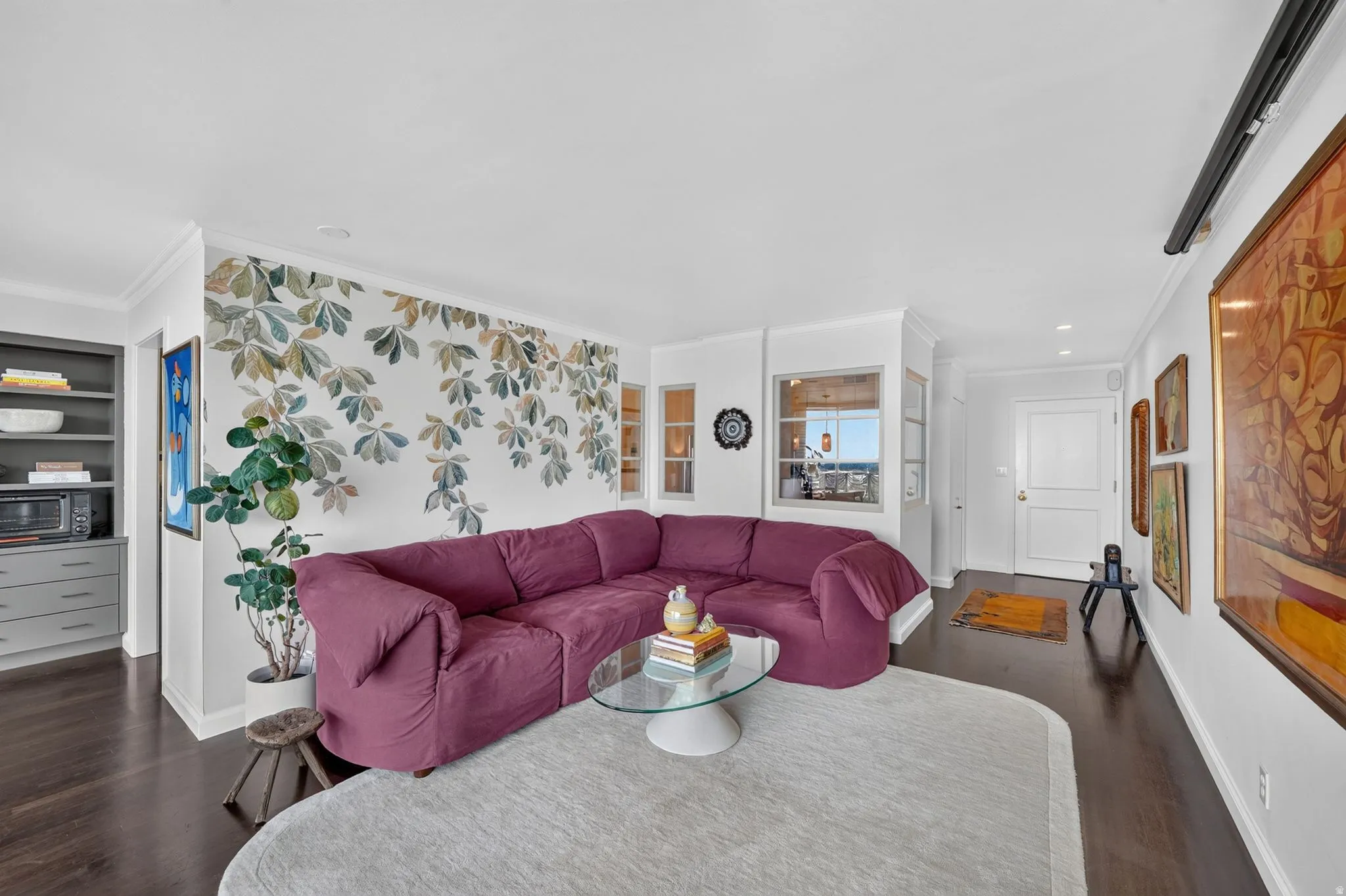 Living area featuring dark wood-finish flooring, white walls, and a decorative botanical accent wall