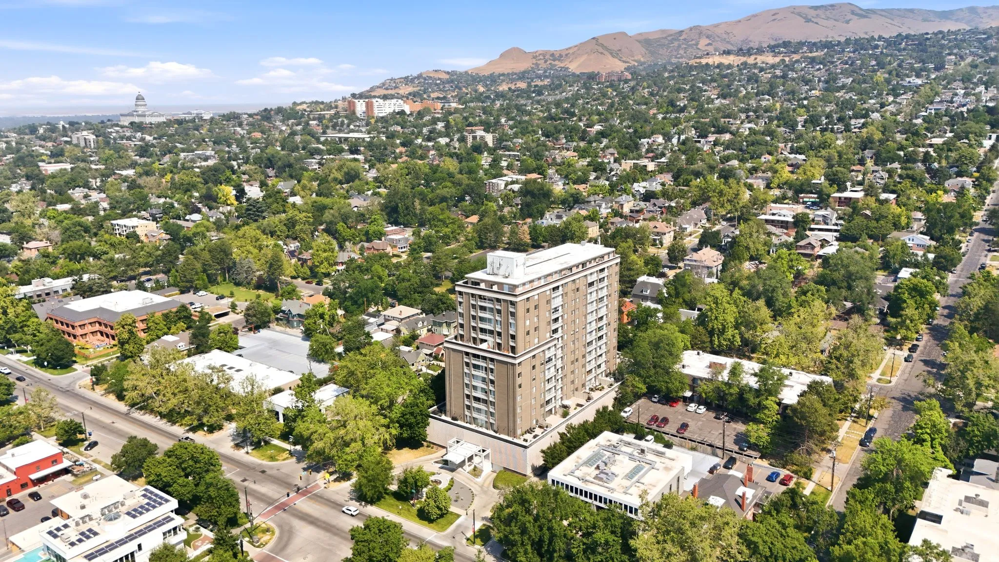 High-rise residential building featuring a light-colored facade with balconies, surrounded by mature trees and a vibrant urban landscape