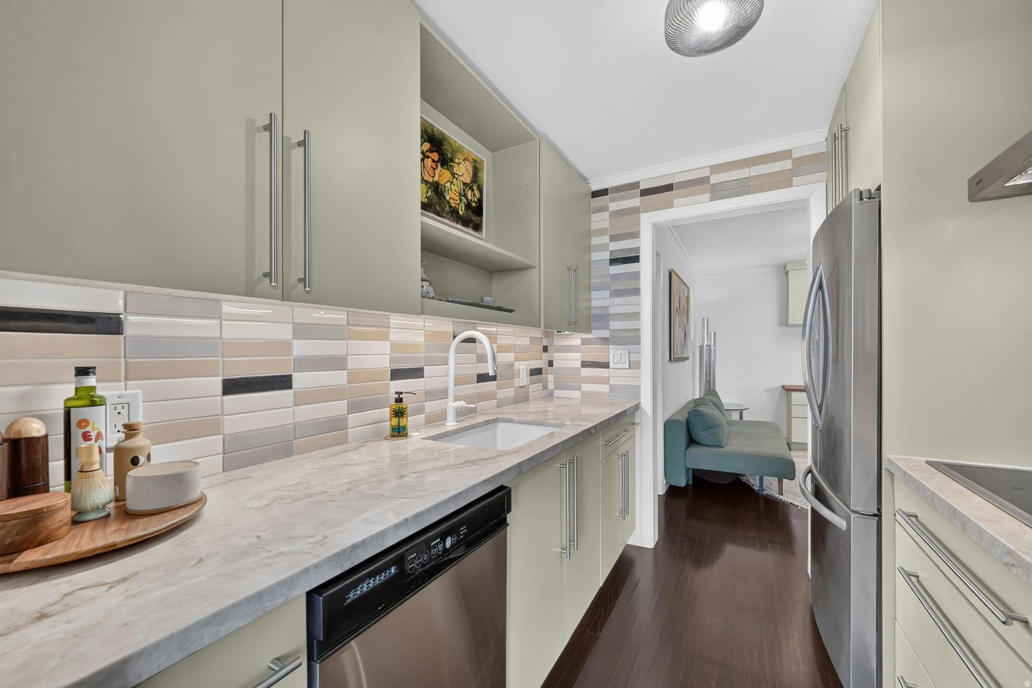 Contemporary kitchen featuring sage-toned cabinetry with brushed nickel hardware, a pristine white sink with a gooseneck faucet, and a multi-toned horizontal tile backsplash