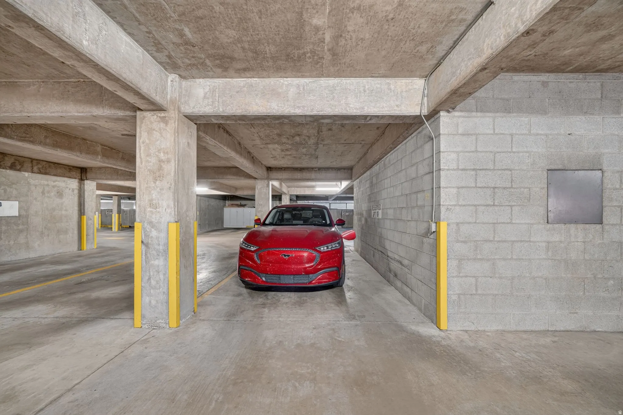 Dedicated parking space within a concrete structure, featuring concrete flooring, concrete block walls, and overhead concrete beams