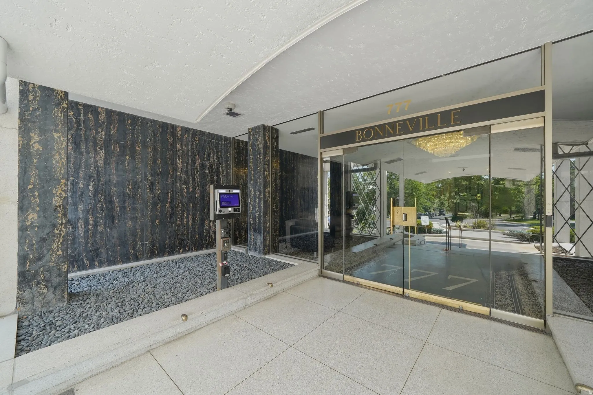 Building entrance featuring automatic glass doors with gold-toned trim, a dark stone accent wall, and a decorative gravel bed