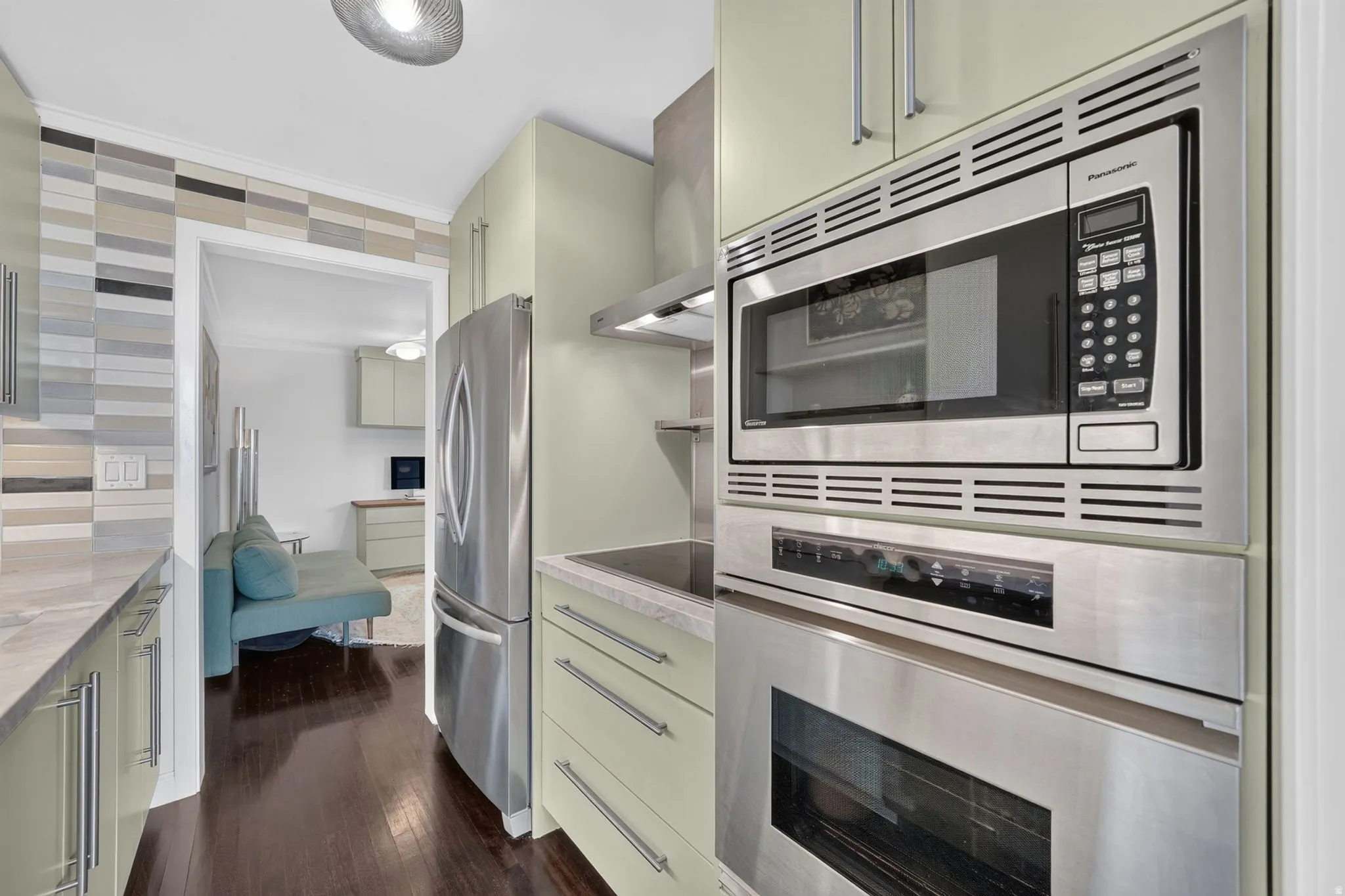 Kitchen featuring stainless steel appliances, light green cabinetry with brushed nickel hardware, light-toned countertop, and a tiled backsplash