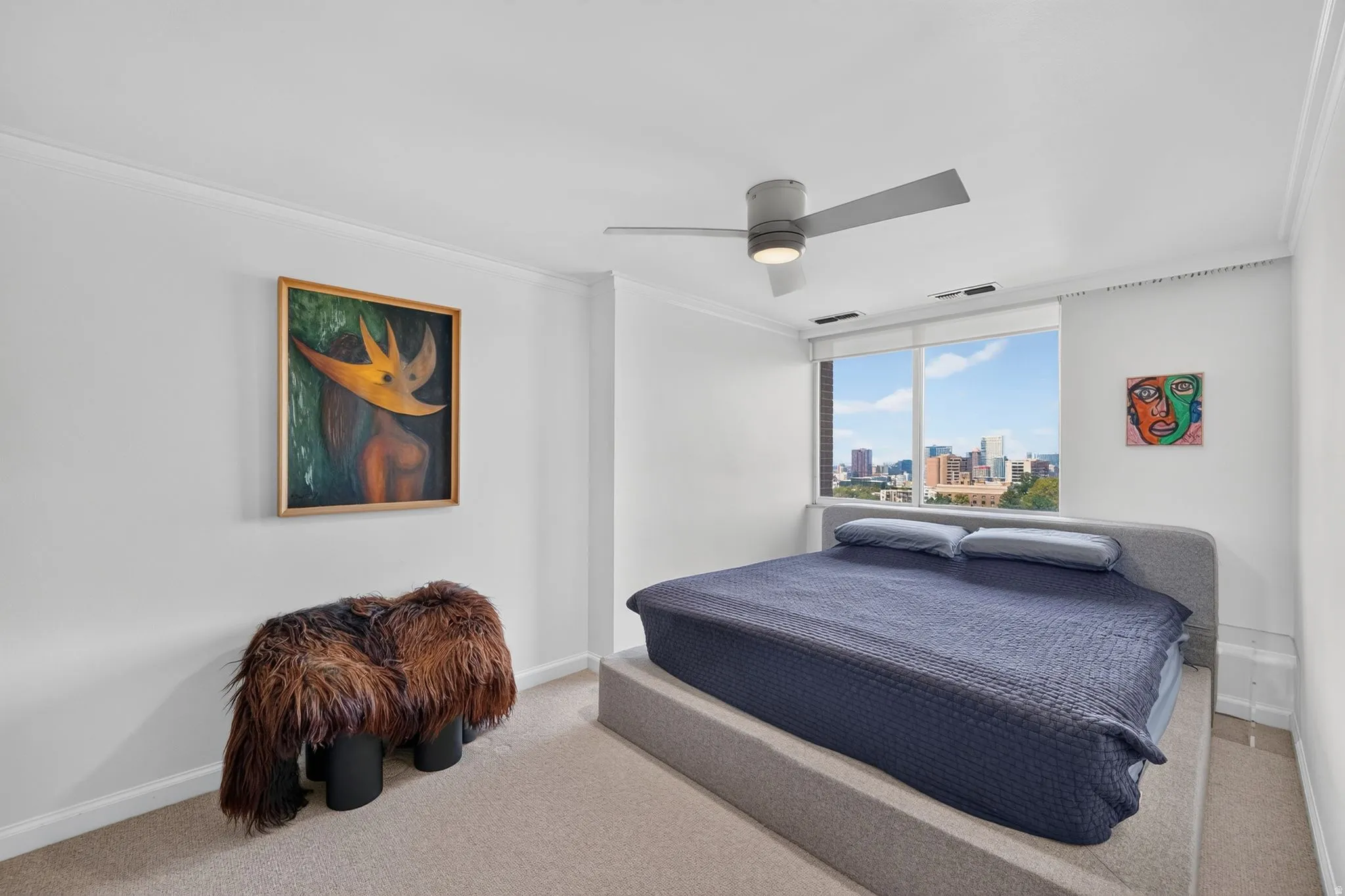 Bright interior featuring a ceiling fan with integrated lighting, wall-to-wall carpeting, and a window with city and sky scenery