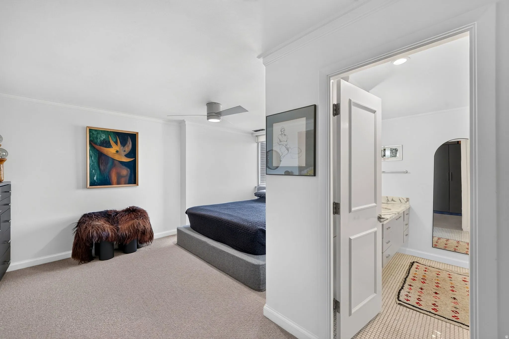 Carpeted sleeping area with a modern ceiling fan, offering direct access to an attached bathroom featuring a tile floor and a vanity with a countertop