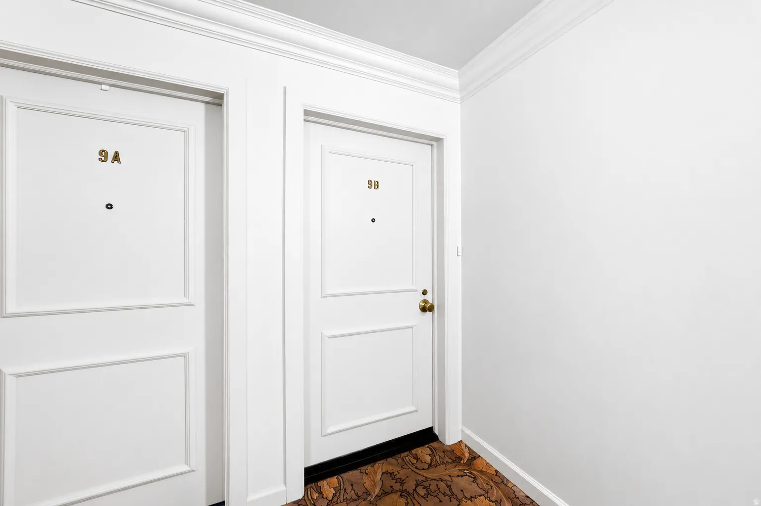 Hallway featuring two panel doors with brass hardware, crown molding, and a patterned floor