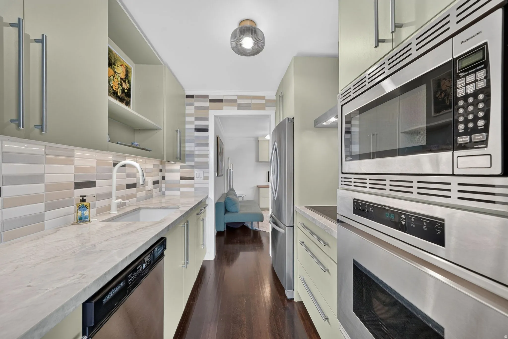 Galley kitchen featuring light green cabinetry, integrated stainless steel appliances, and wood-finish flooring
