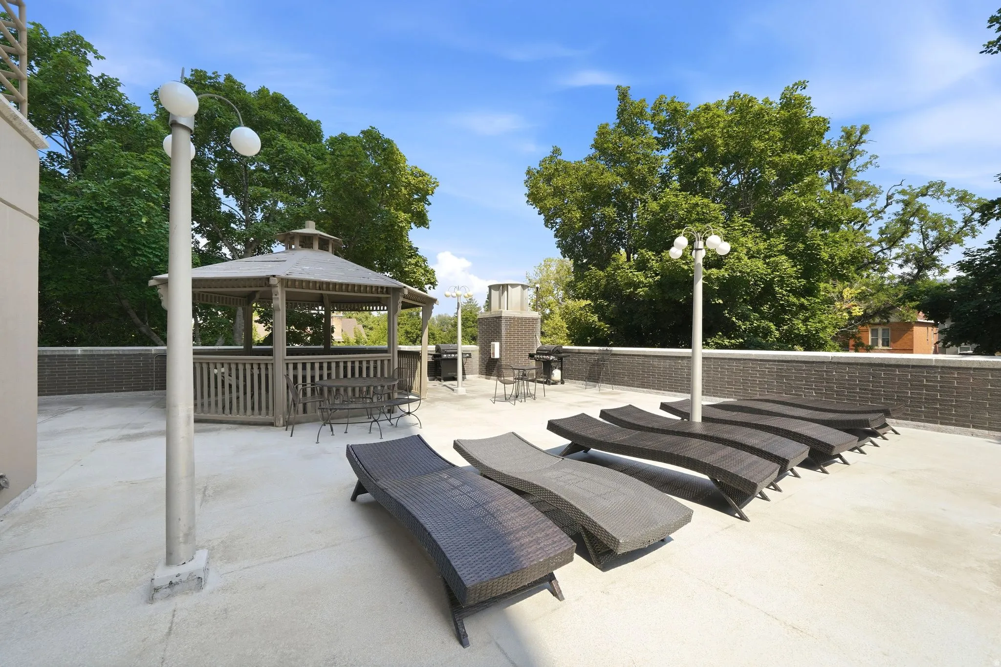 Rooftop deck featuring a wooden gazebo, a brick-patterned wall, multiple light fixtures, and a clear sky above