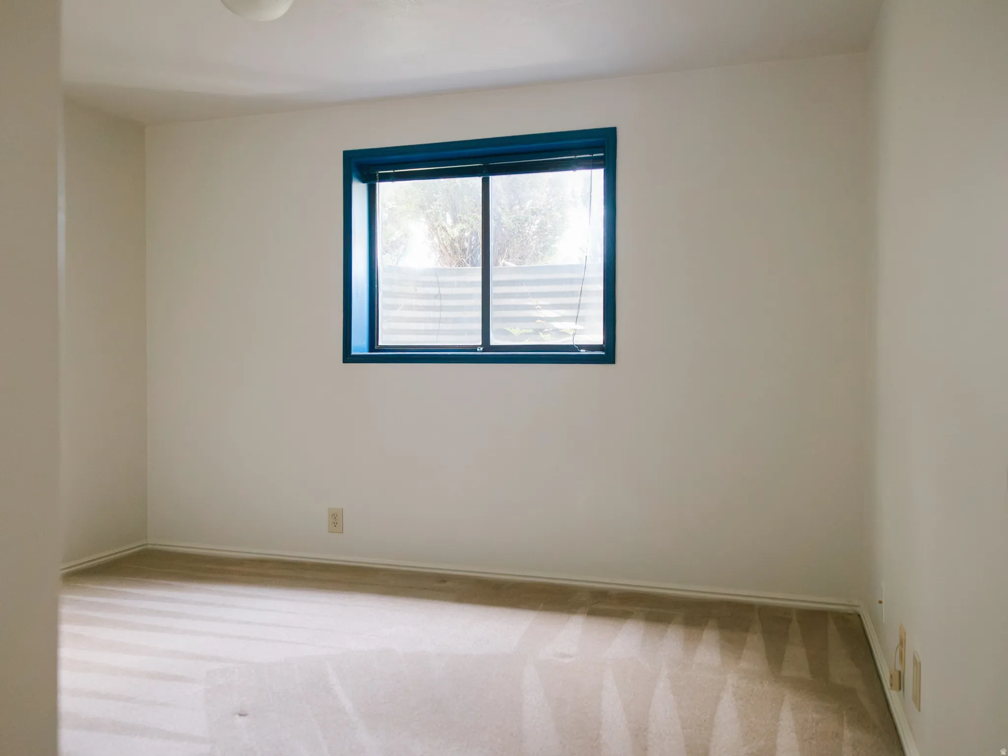 Room with a blue-framed window, neutral wall paint, and light-toned patterned carpeting