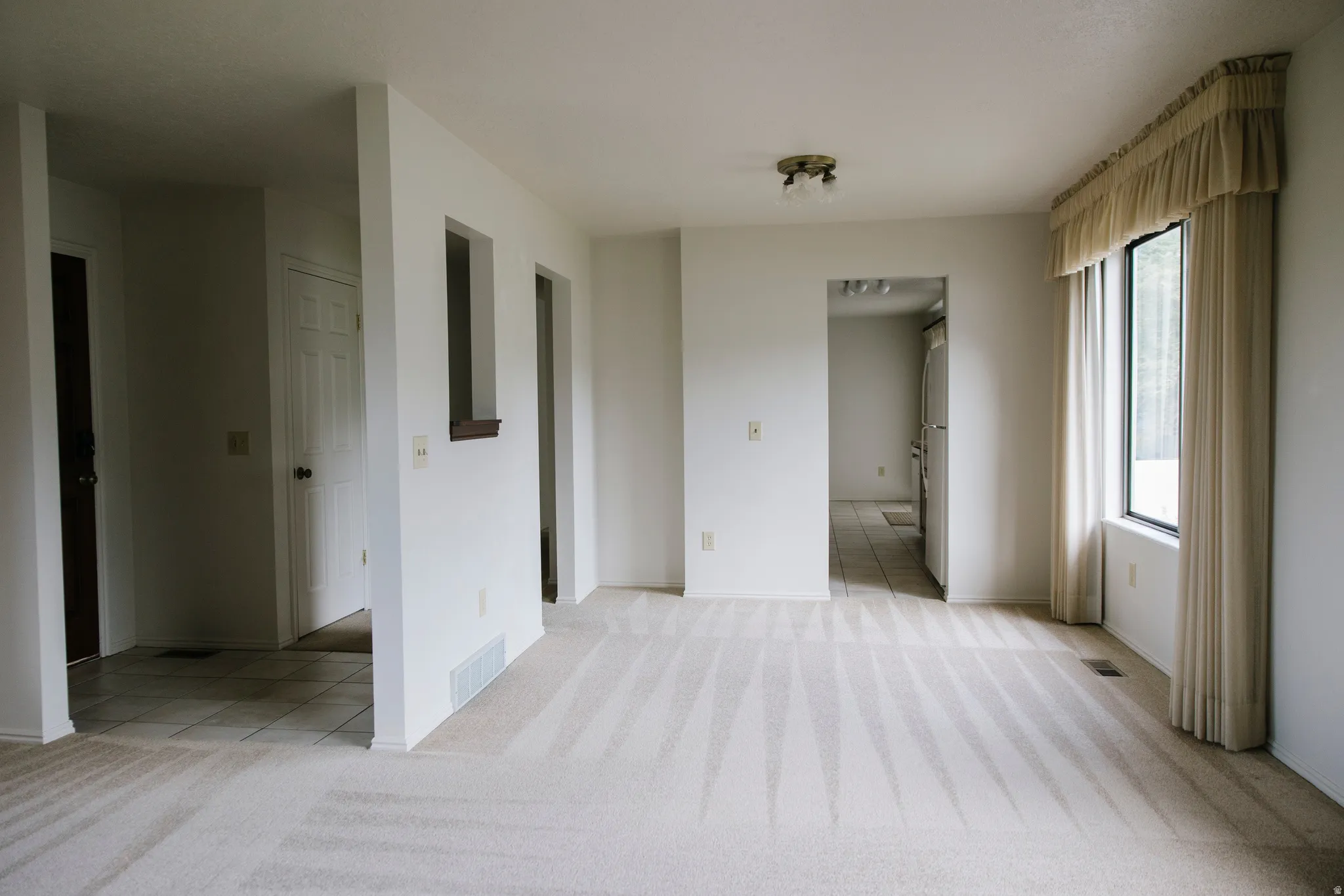 Carpeted living area featuring a large window, a ceiling-mounted light fixture, and white wall finishes