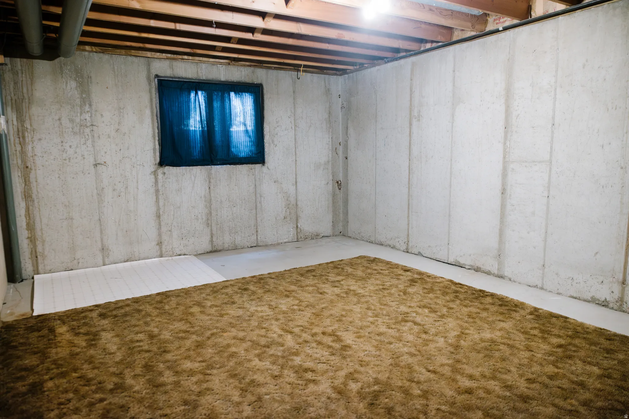 Unfinished basement space featuring exposed wood joists and concrete walls