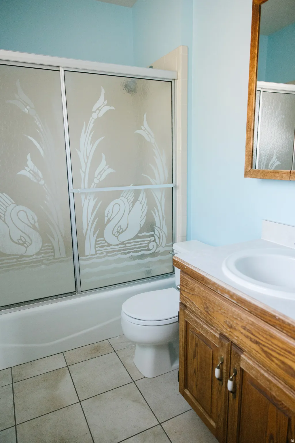 Bathroom featuring a sliding glass shower door with etched design, a white bathtub, a toilet, a wood-finish vanity with an integrated sink, and square floor tiles