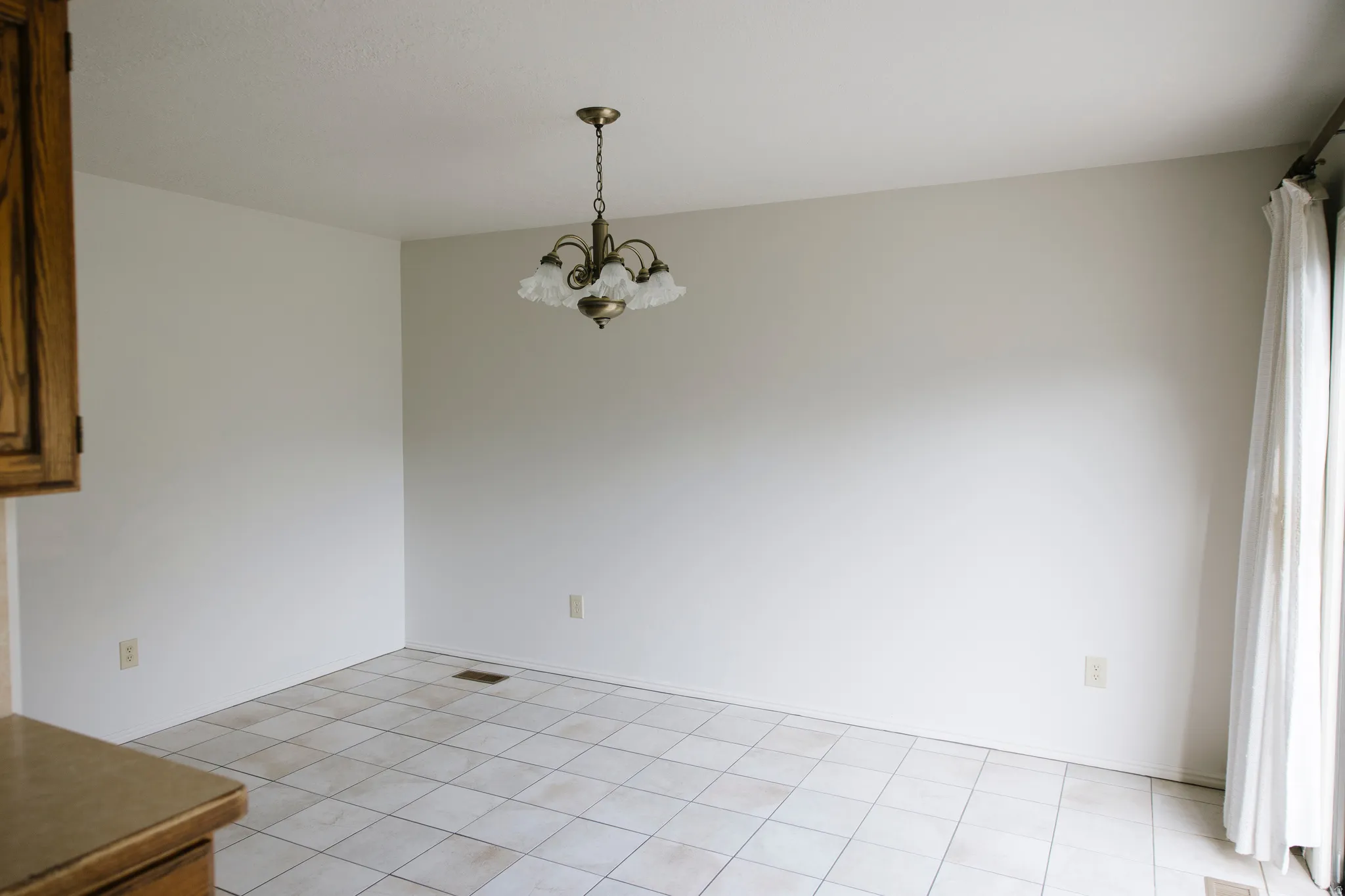 Room featuring white tile flooring, neutral wall tones, and a brass-finish chandelier with frosted glass shades