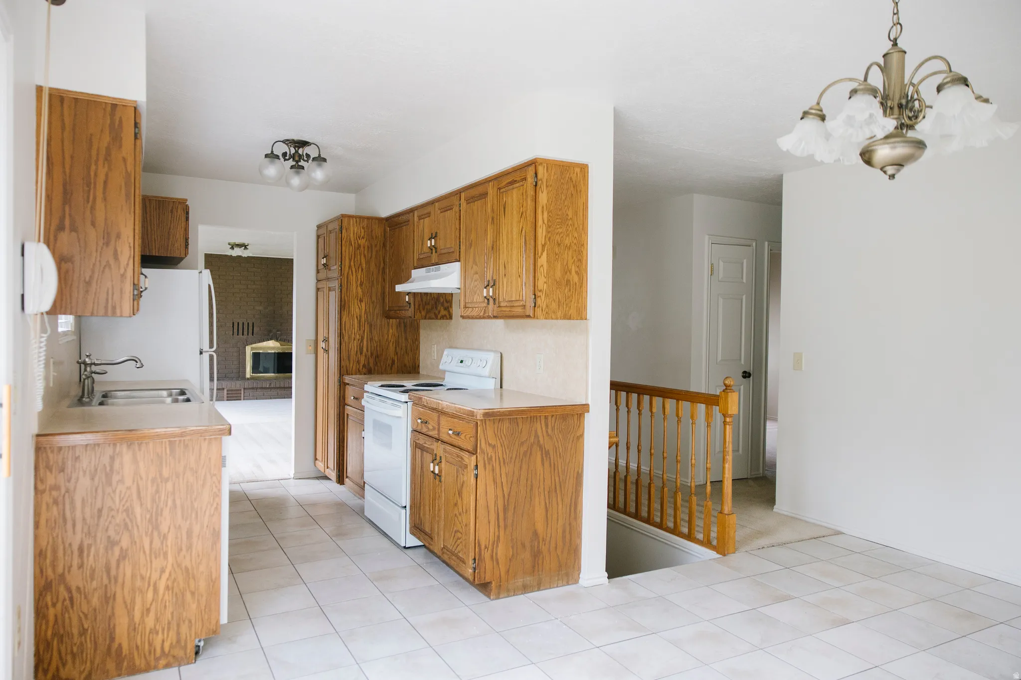Kitchen featuring oak-finish cabinetry, light-toned countertops, and white appliances