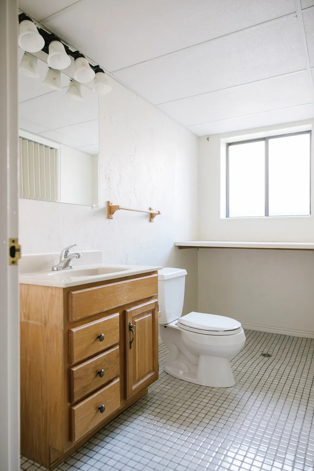Bathroom featuring a wooden vanity with integrated sink, white tile flooring, contemporary lighting fixture, and a window for natural light