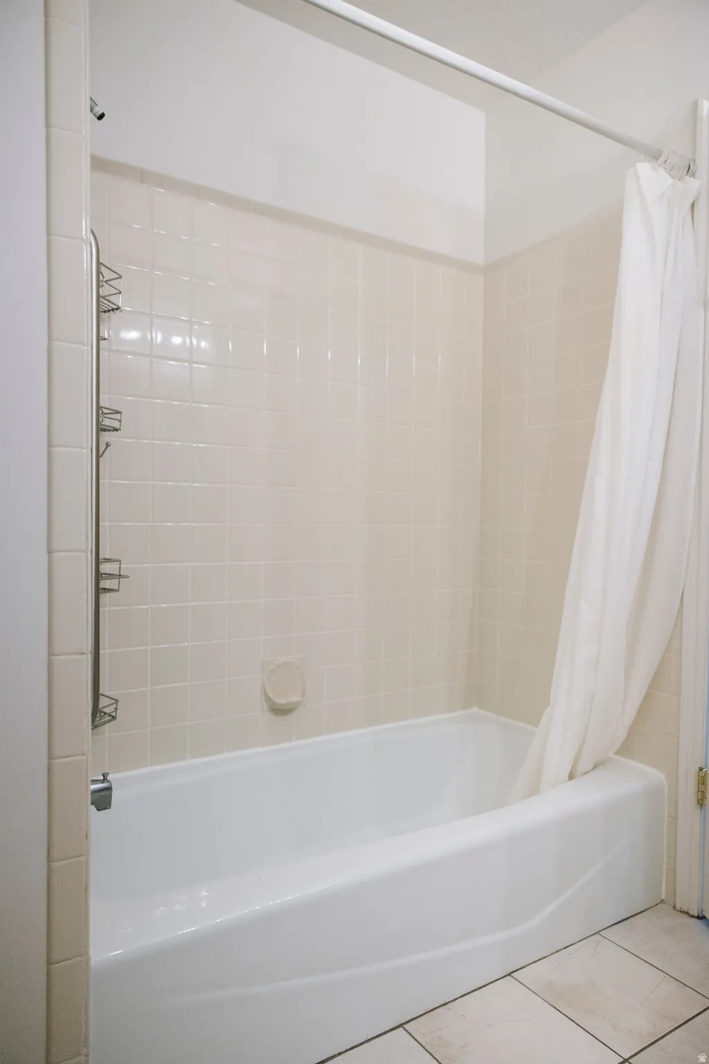 Bathtub with white tile surround, a built-in soap dish, and a shower head with an attached caddy