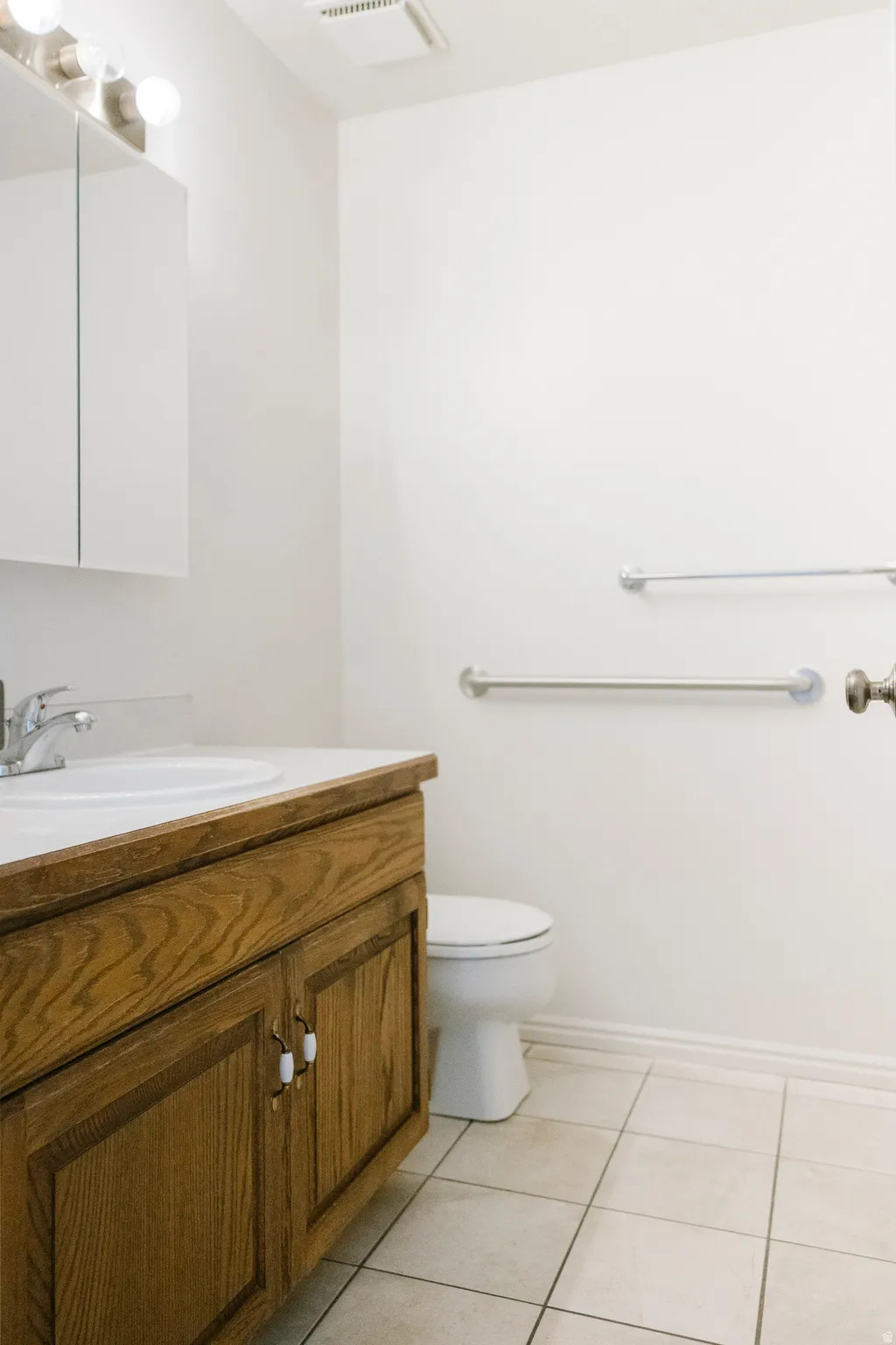 Bathroom featuring a wooden vanity with a white countertop and integrated sink, a wall-mounted medicine cabinet with mirror doors, and overhead lighting
