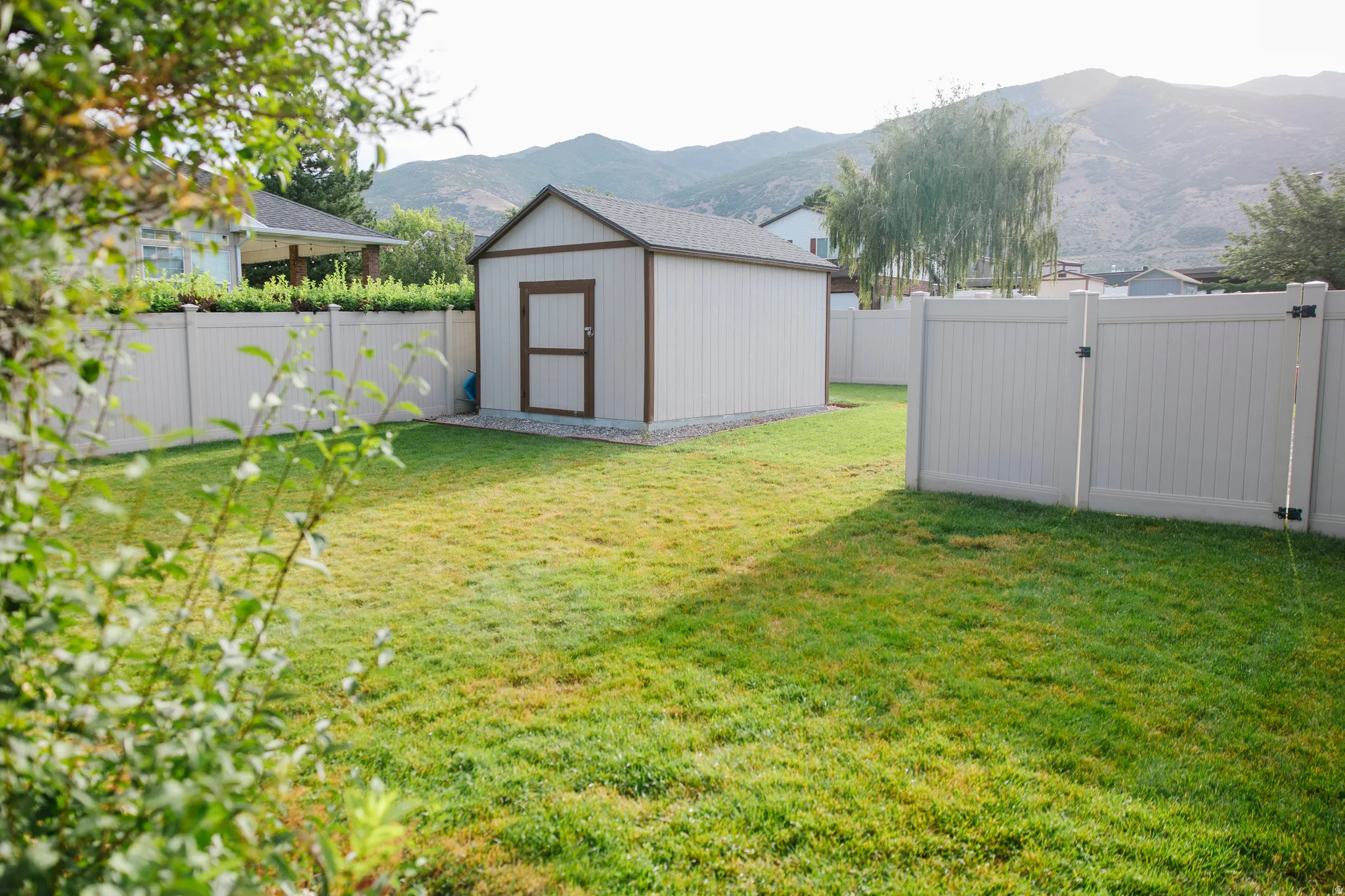Spacious yard featuring a detached storage shed with a brown-trimmed door, full vinyl fencing, and a mountain backdrop