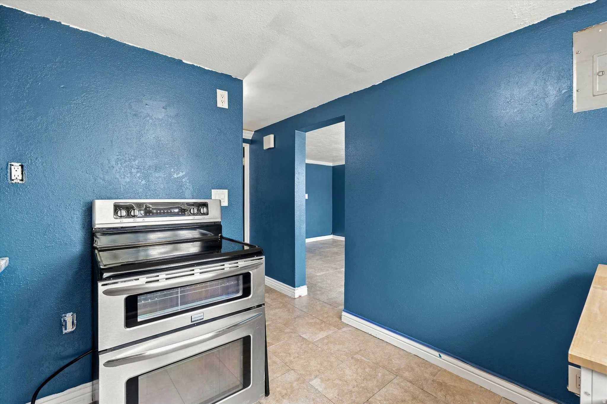 Stainless steel range with double ovens, blue wall finish, and tiled flooring