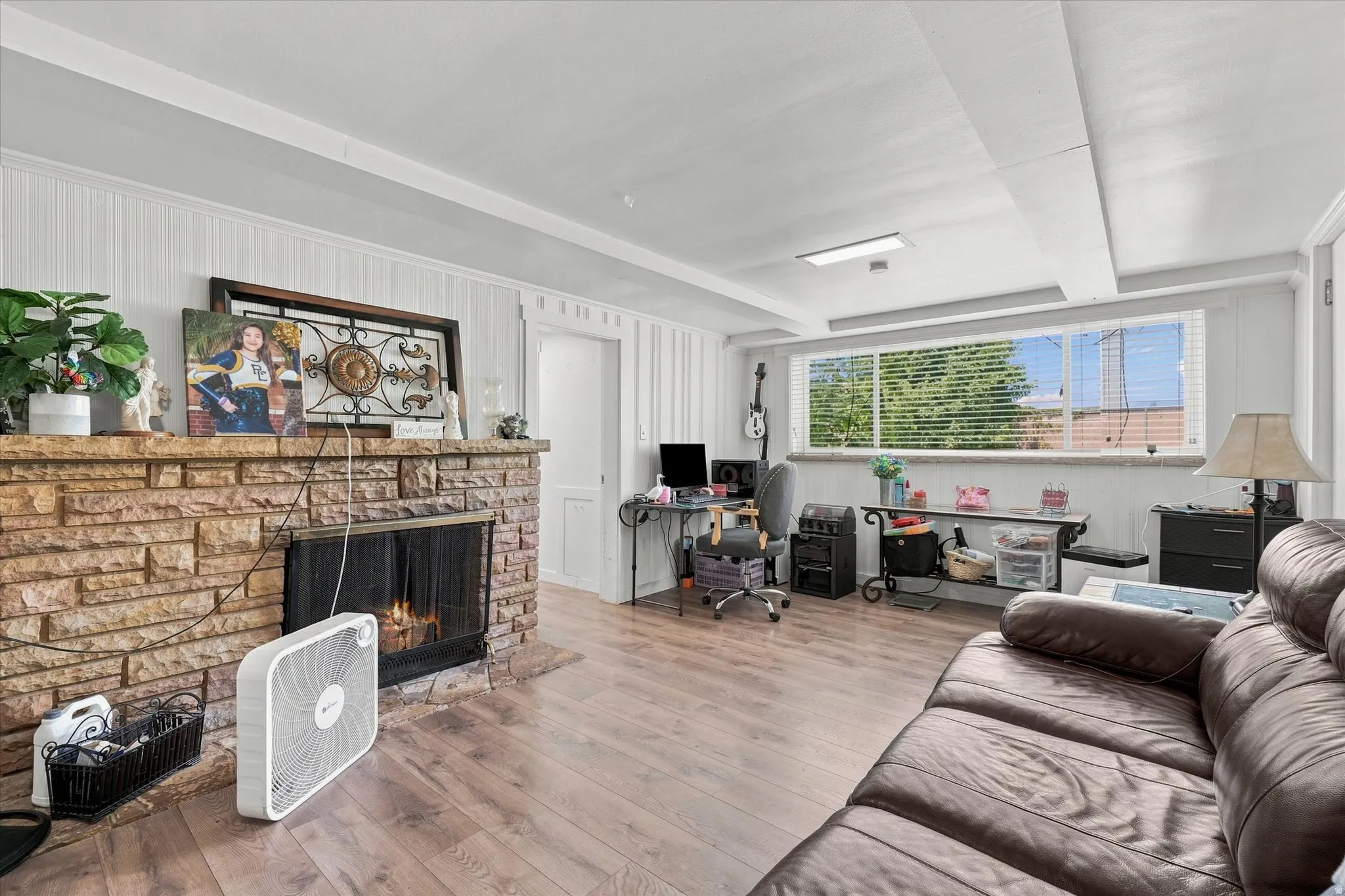 Stone-clad fireplace with a hearth, wood-finish flooring, and natural light from a window with blinds