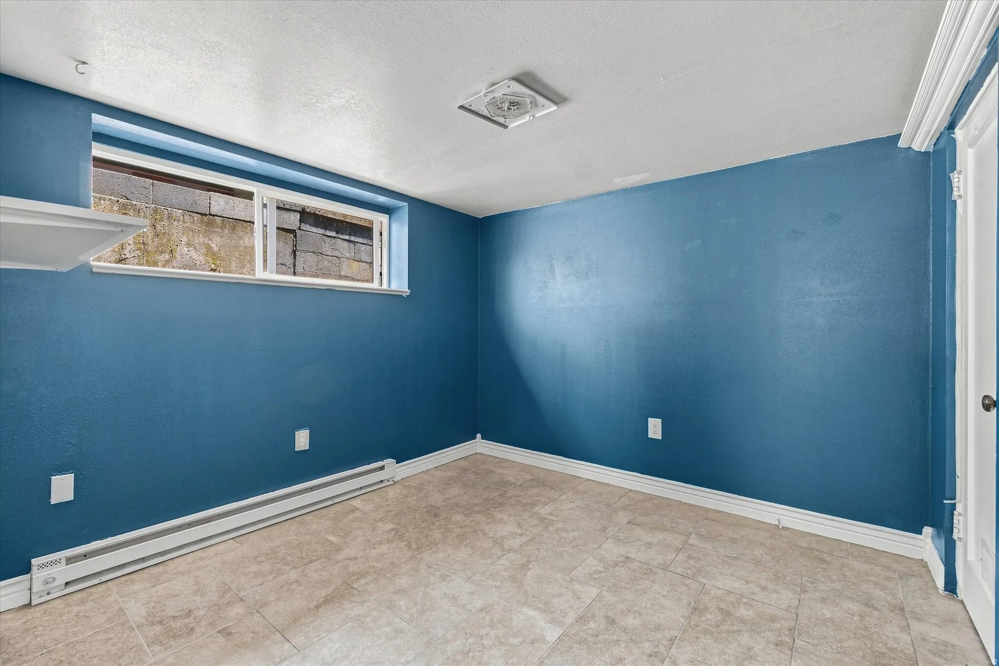 Room featuring blue painted walls, neutral-toned tile flooring, a horizontal sliding window, and a white interior door with crown molding