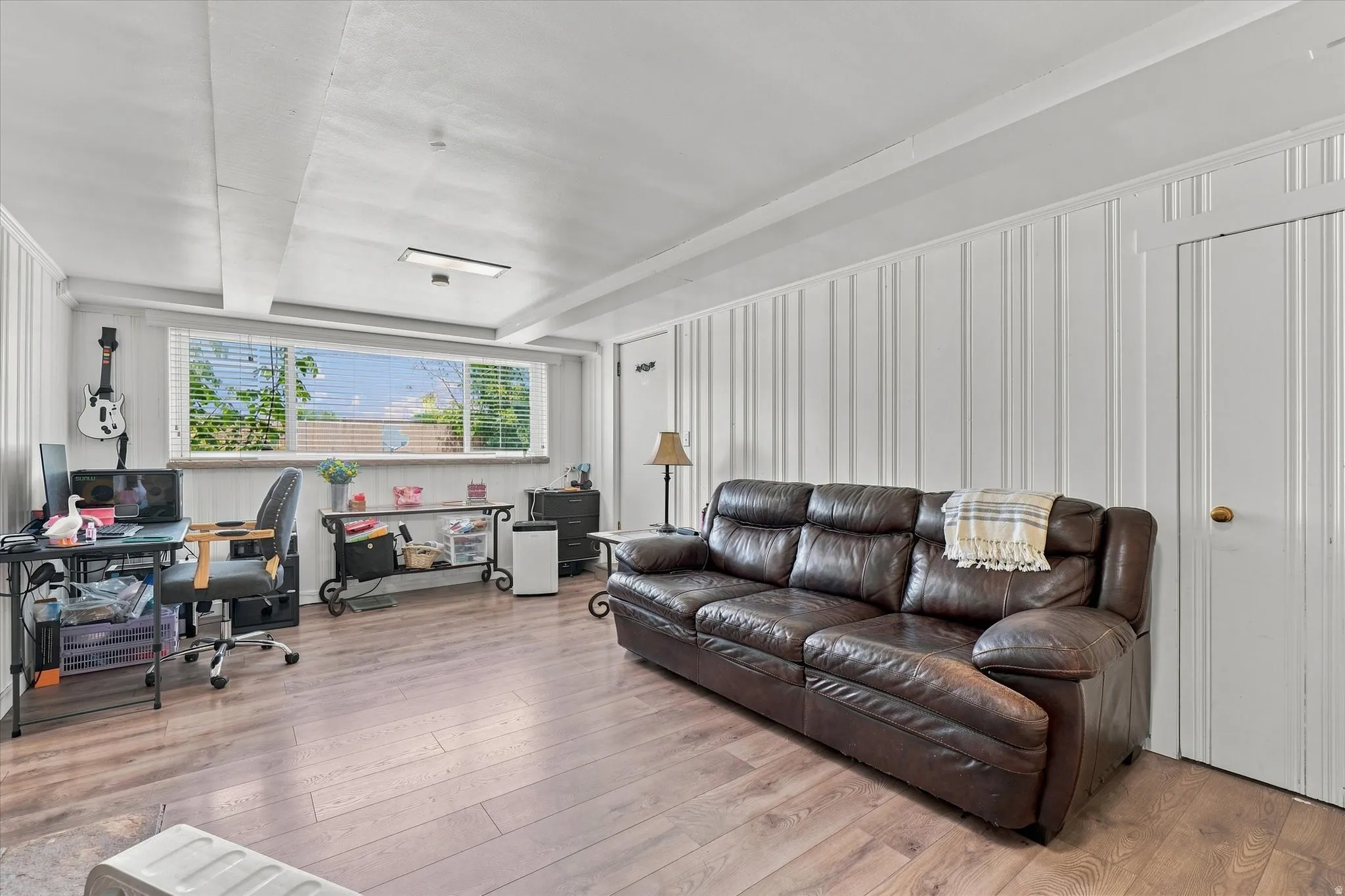 Expansive room featuring wood-finish flooring, white board and batten wall paneling, and an extended window