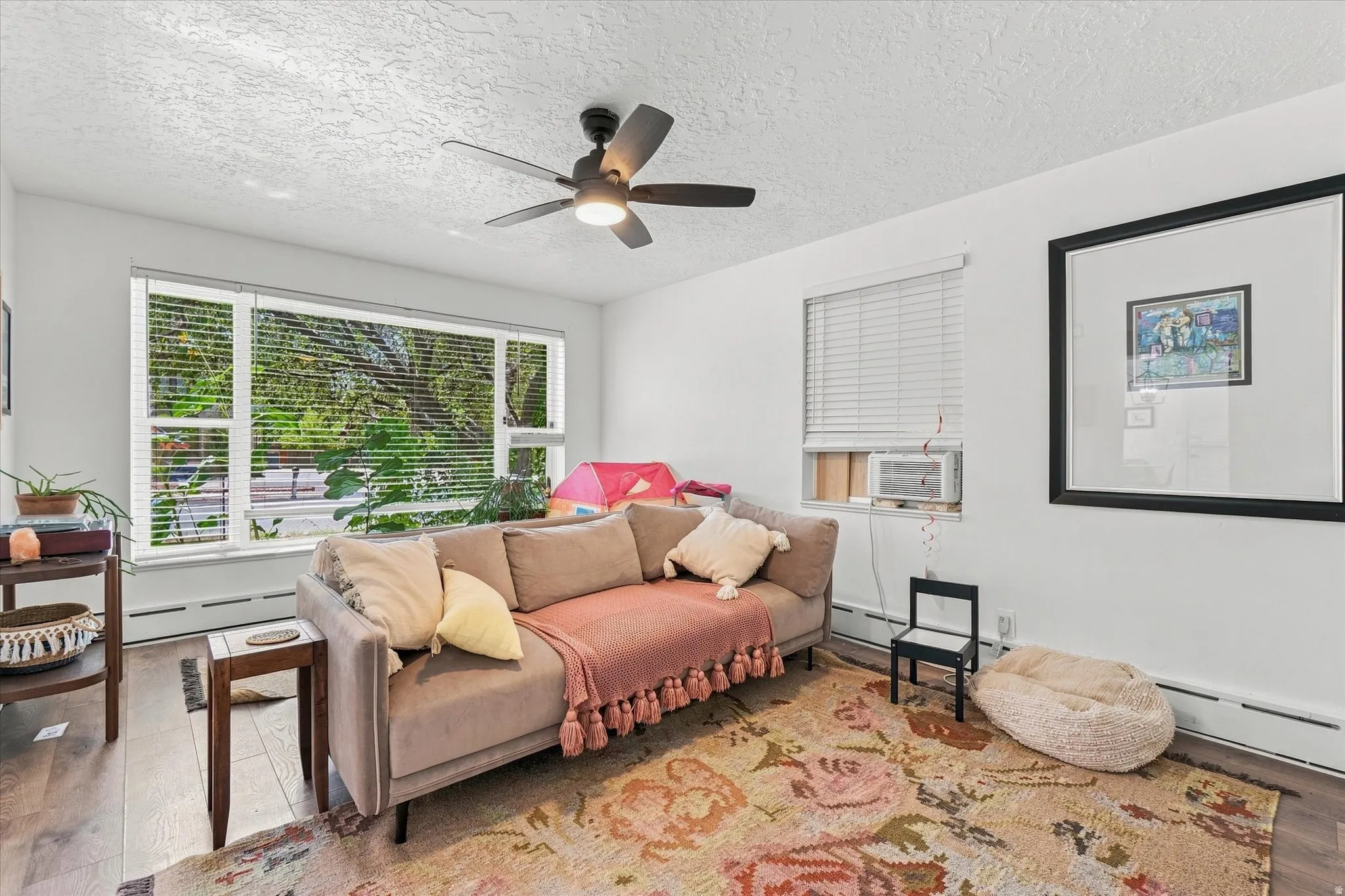 Hardwood-finish flooring, a ceiling fan with integrated lighting, and multiple windows providing natural light