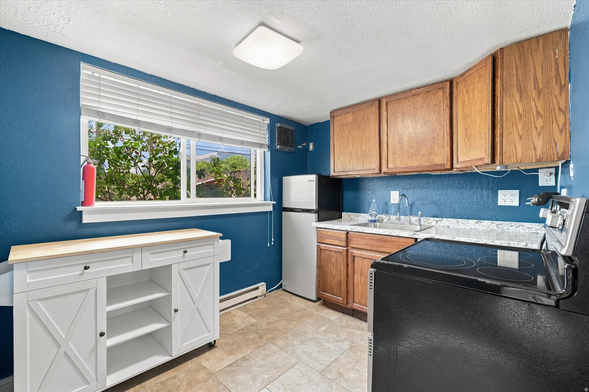 Kitchen featuring wood-finish cabinetry, a stainless steel sink, a refrigerator, and a black electric range