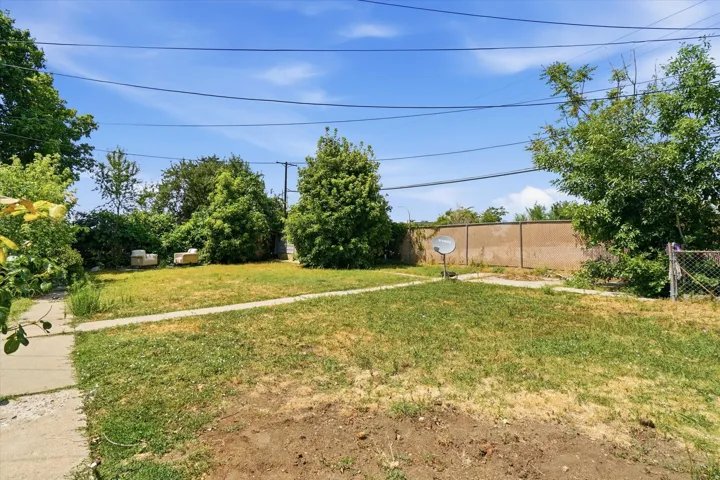 Expansive backyard featuring a partial concrete pathway, mature trees, and a concrete perimeter wall