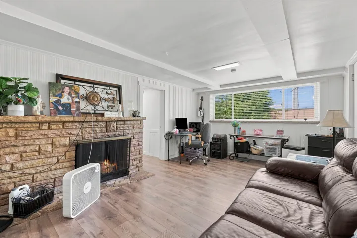 Stone-clad fireplace with a hearth, wood-finish flooring, and natural light from a window with blinds