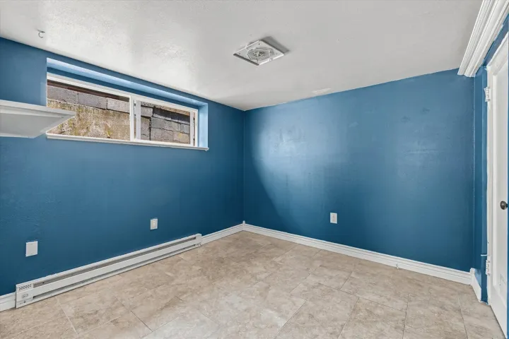 Room featuring blue painted walls, neutral-toned tile flooring, a horizontal sliding window, and a white interior door with crown molding