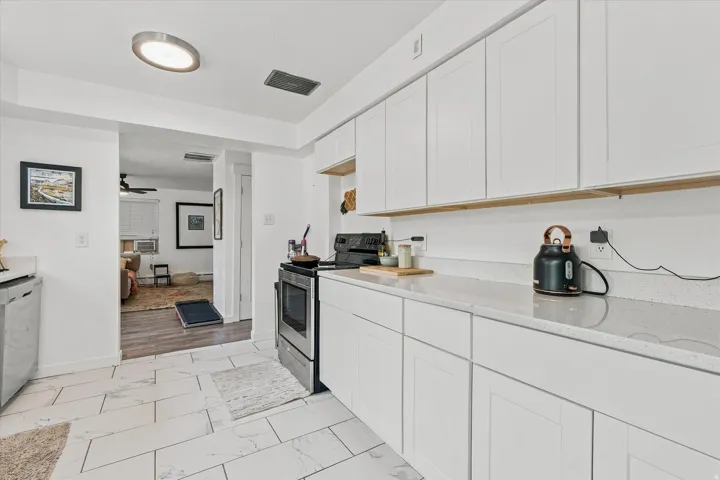 White flat-panel cabinetry with light wood-finish accents, light-toned countertops, tile flooring, and stainless steel appliances
