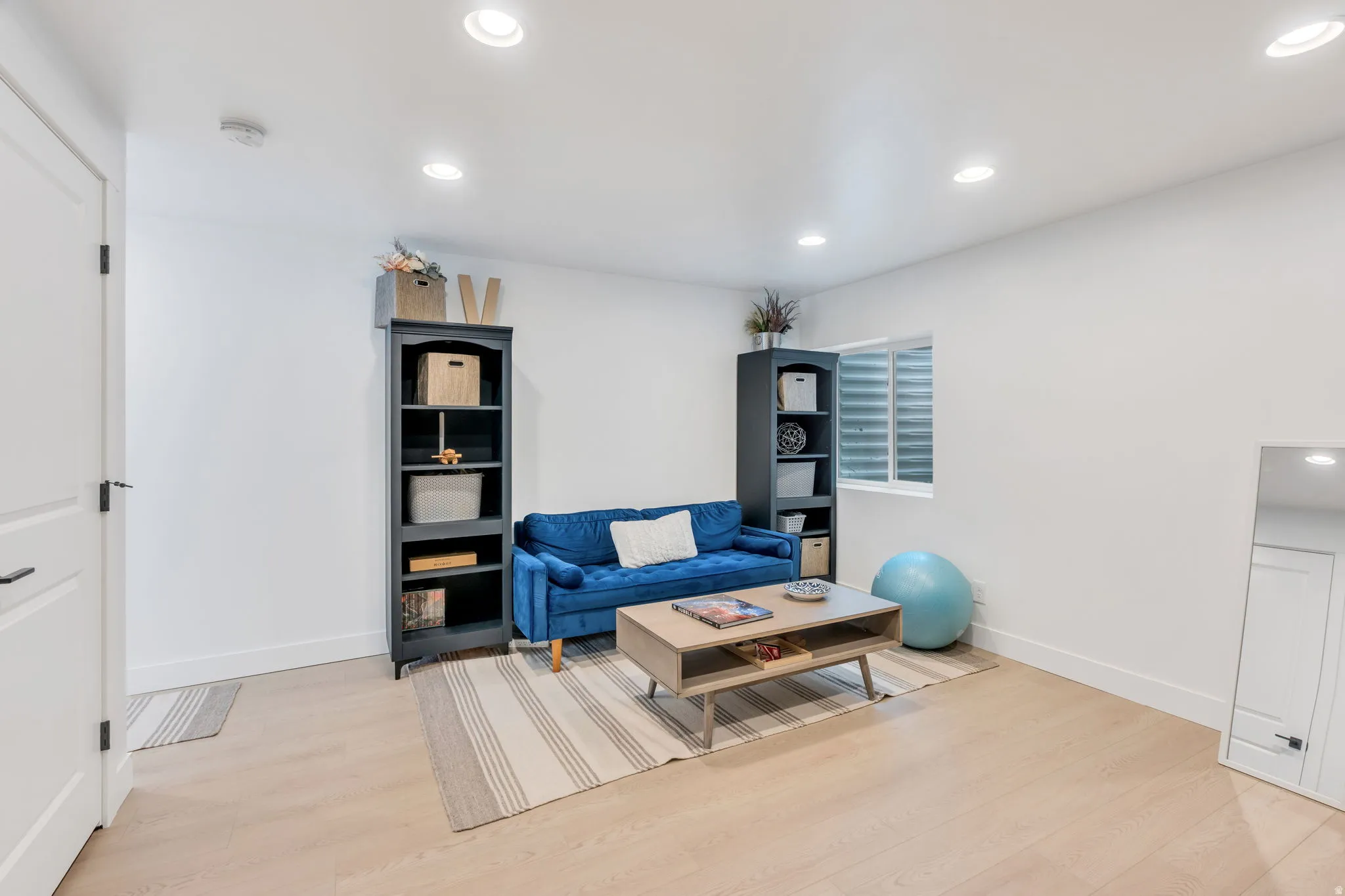 Spacious room featuring light wood-finish flooring, recessed ceiling lighting, and a white color palette