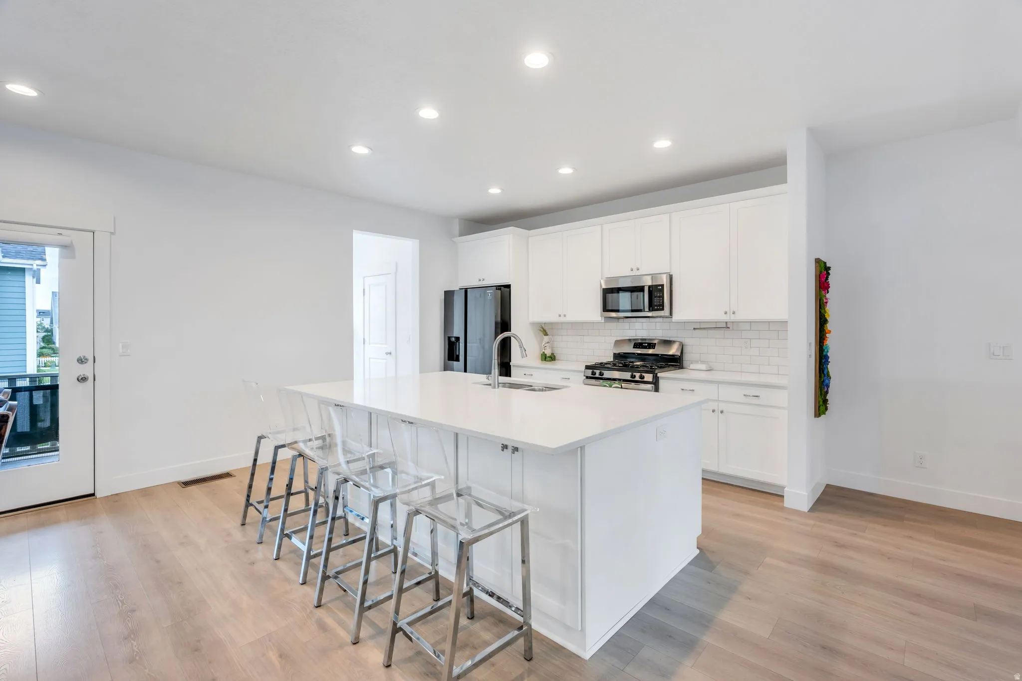 Modern kitchen featuring an expansive center island with seating, white shaker cabinetry, stainless steel appliances, and wood-finish flooring
