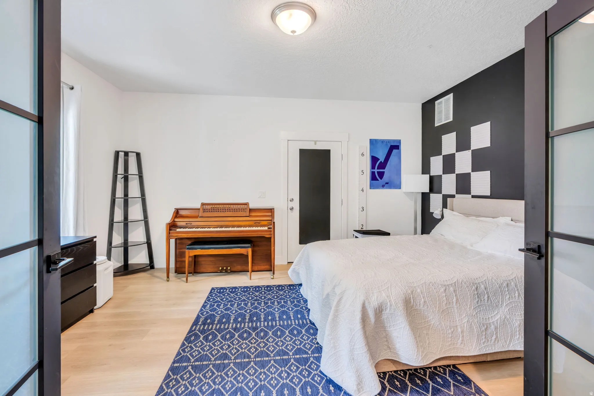 Bedroom featuring light wood-finish flooring, a contemporary ceiling light fixture, and a dark accent wall