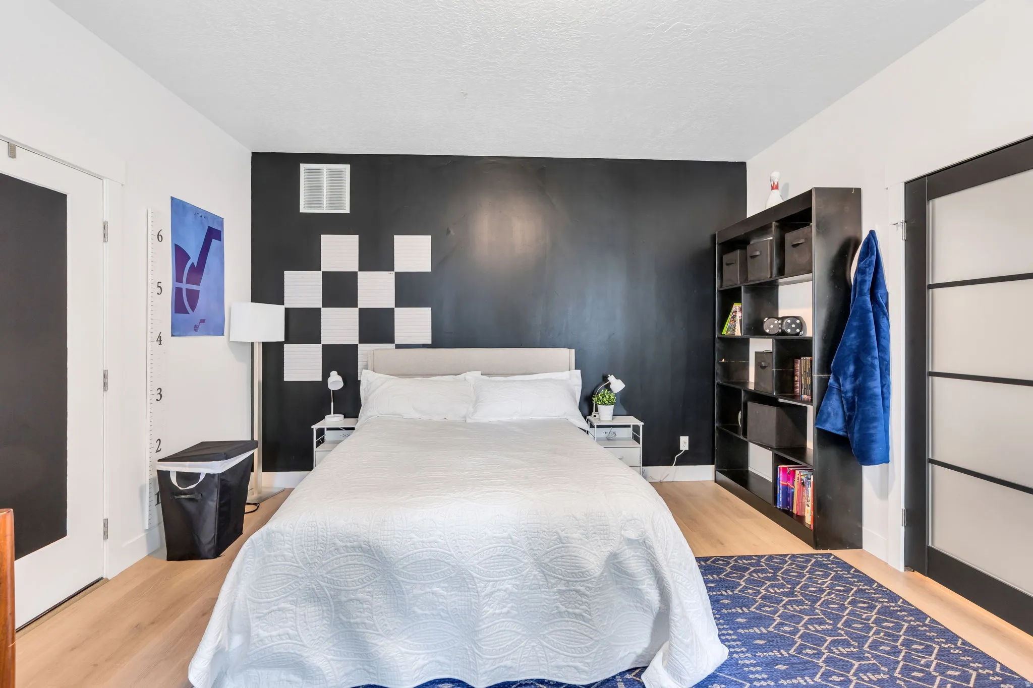Bedroom featuring light wood-finish flooring, a contemporary accent wall with checkerboard detailing, and a black-framed door with frosted glass panels