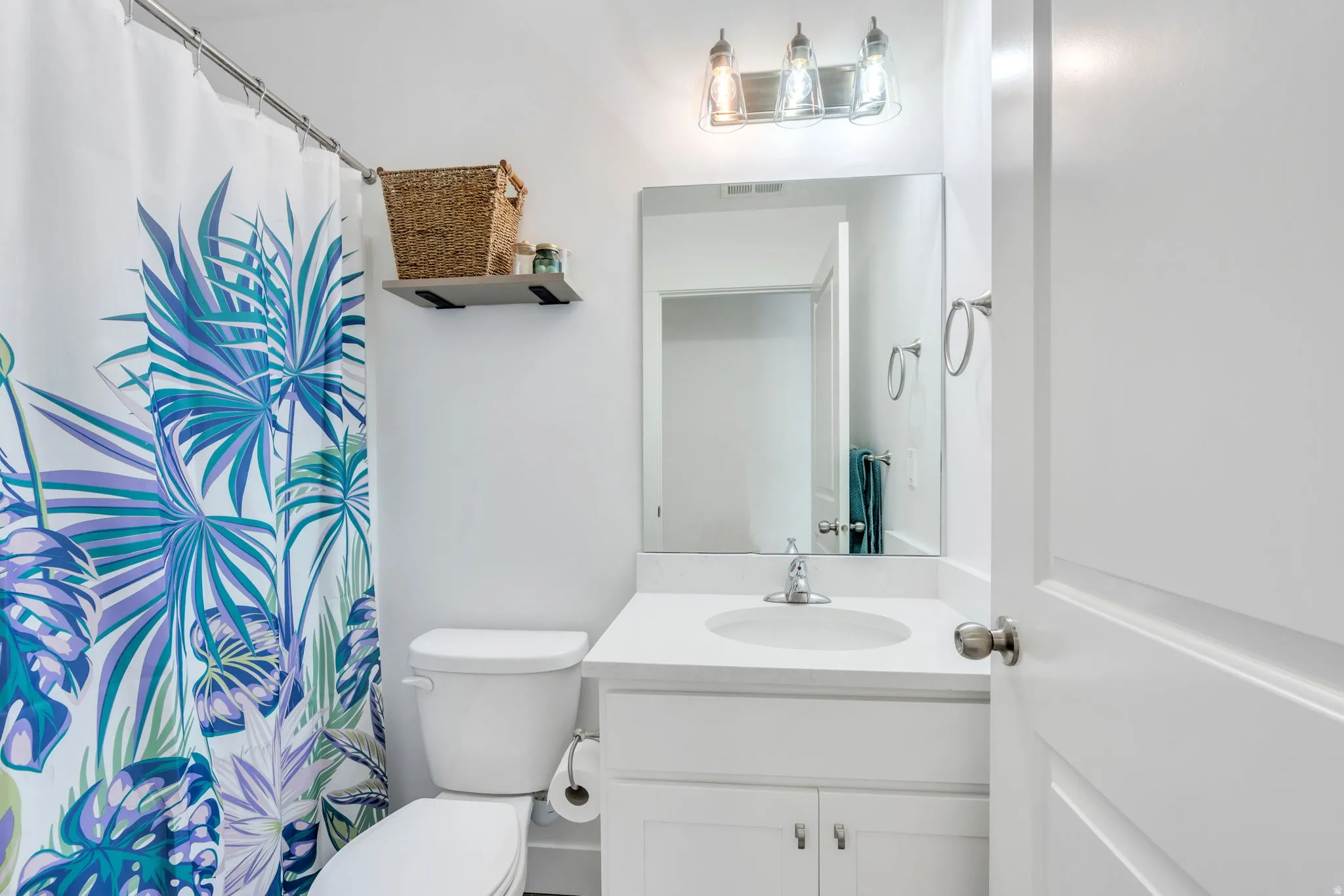 Bright bathroom featuring a single vanity with a white countertop and undermount sink, a framed mirror, and a three-light vanity fixture