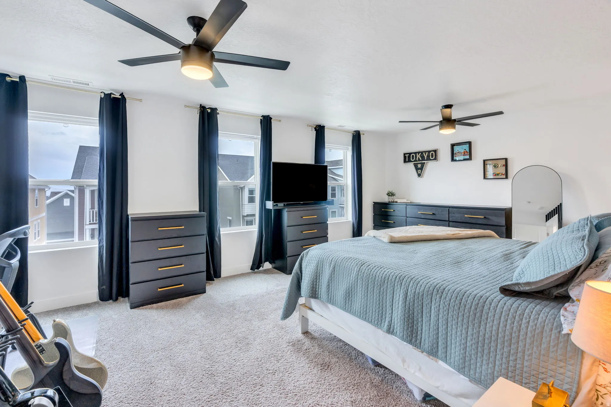 Bright bedroom featuring multiple windows, two ceiling fans with integrated lighting, and carpeted flooring