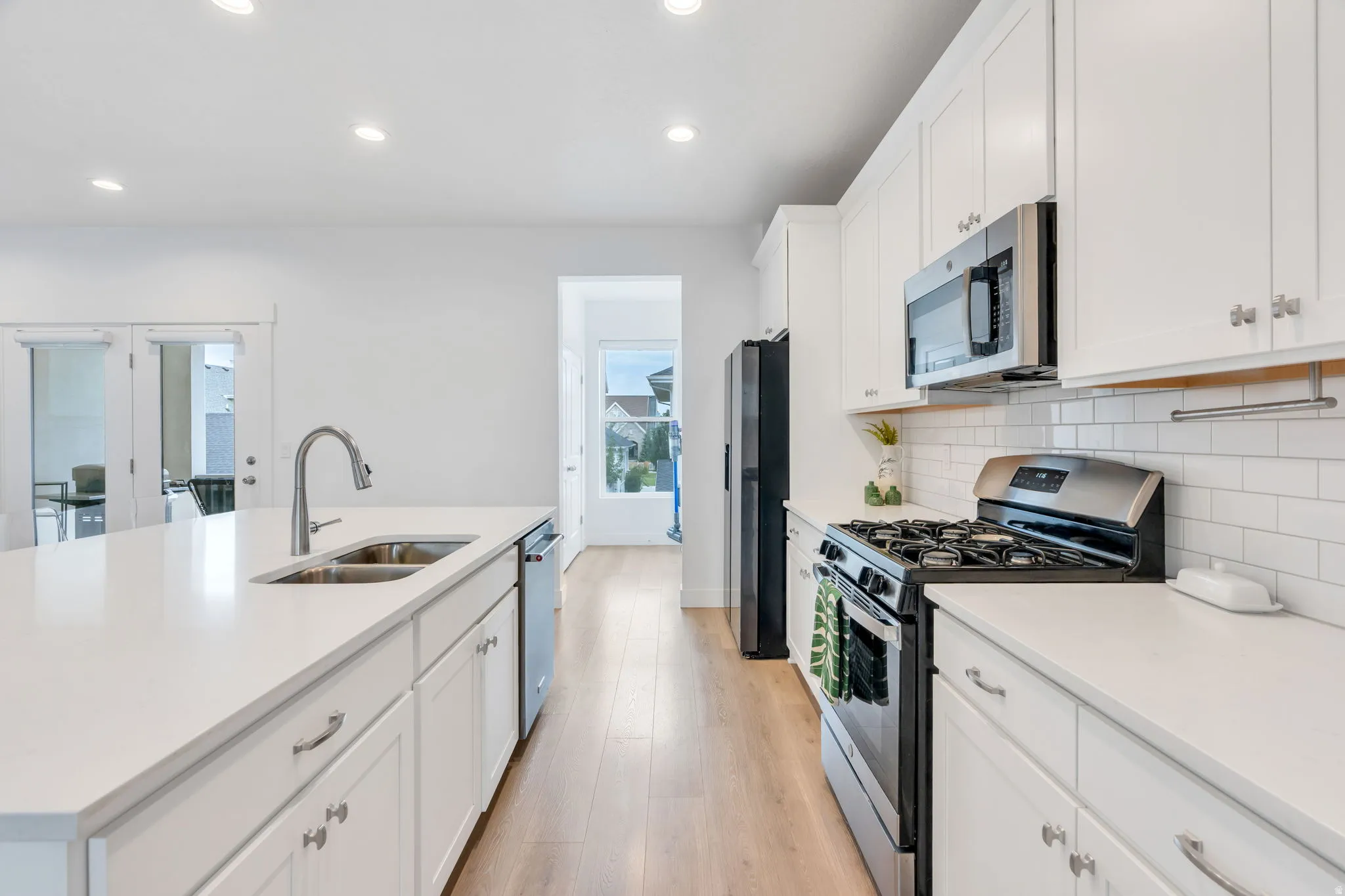 Bright kitchen featuring white cabinetry, light countertops, wood-finish flooring, stainless steel appliances, and a subway tile backsplash