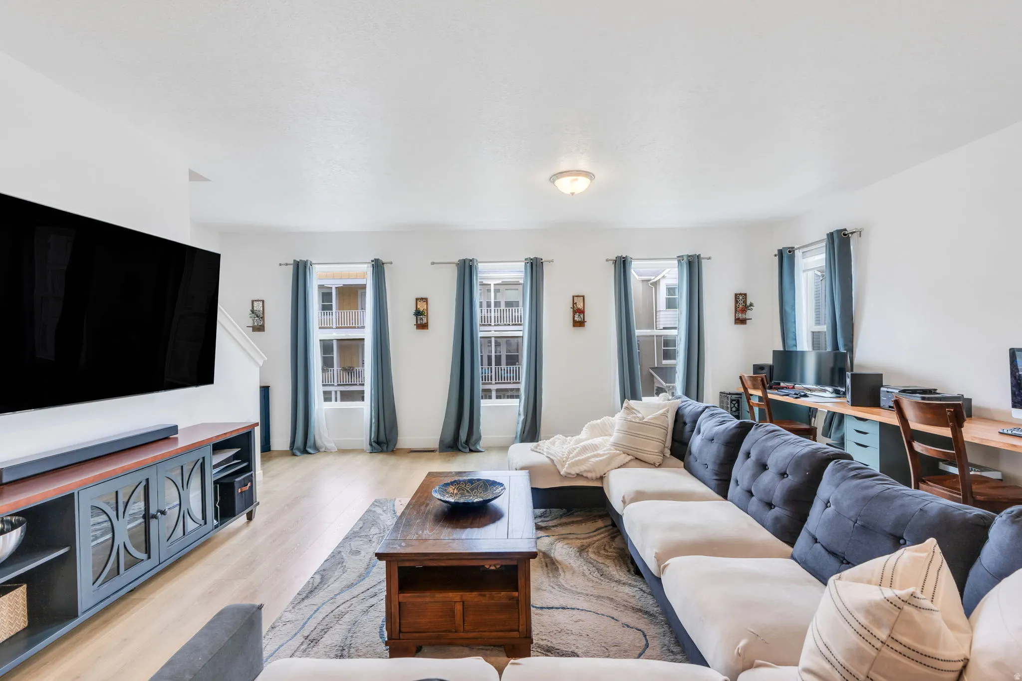 Spacious living area featuring light wood-finish flooring and multiple windows with curtain rods