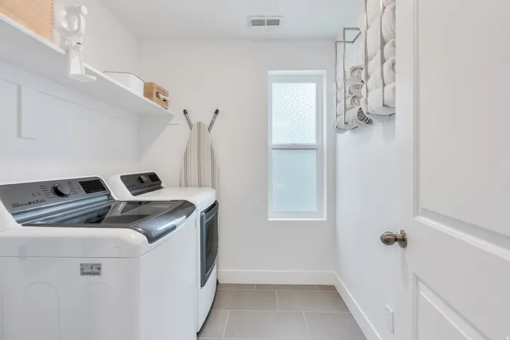 Dedicated laundry space featuring white appliances, open shelving, a frosted window, and gray tile flooring