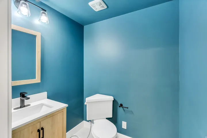 Powder room featuring a wood-finish vanity with a white countertop and integrated sink, matte black faucet, and rectangular framed mirror