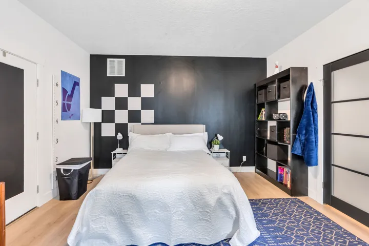 Bedroom featuring light wood-finish flooring, a contemporary accent wall with checkerboard detailing, and a black-framed door with frosted glass panels