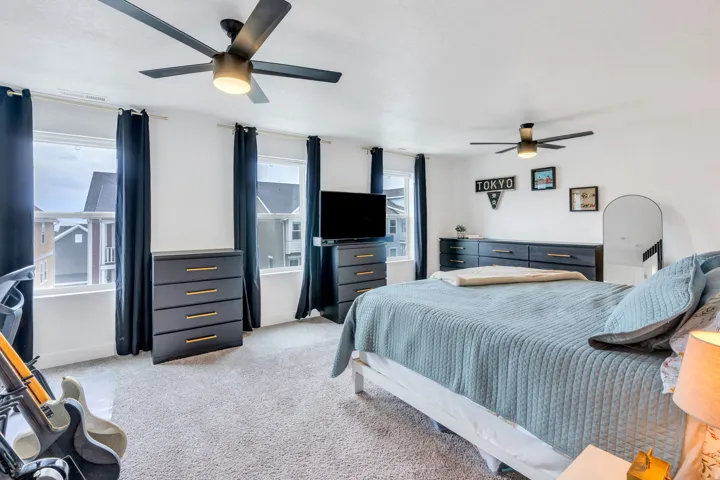 Bright bedroom featuring multiple windows, two ceiling fans with integrated lighting, and carpeted flooring