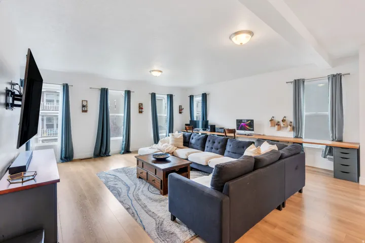 Spacious living area featuring light wood-finish flooring, multiple windows providing natural illumination, and a built-in desk spanning the far wall