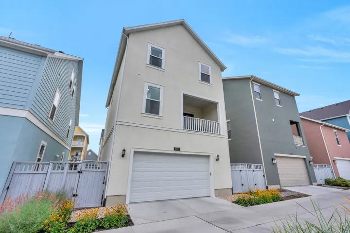 Three-story stucco exterior featuring a built-in garage, second-story balcony with white railing, and multiple windows