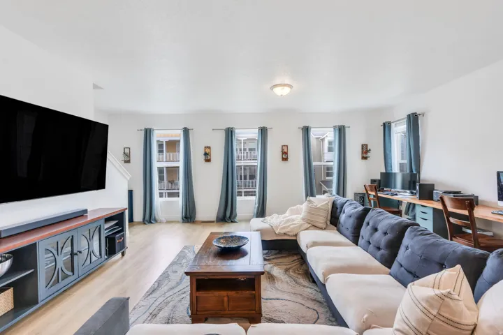 Spacious living area featuring light wood-finish flooring and multiple windows with curtain rods