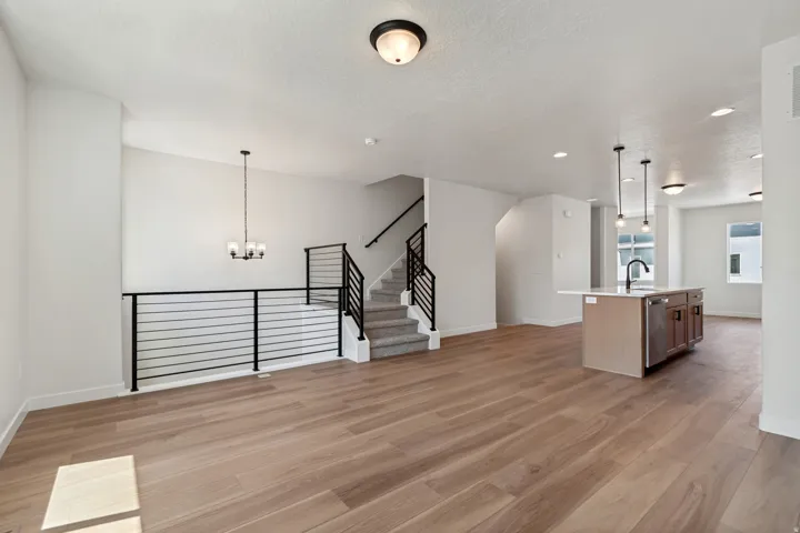 Open-concept living area featuring wide-plank wood-finish flooring, a modern black metal horizontal railing, and a central kitchen island with a white countertop and dark base cabinetry