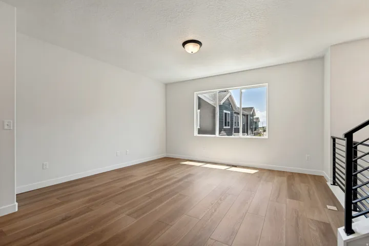 Spacious room featuring wood-finish flooring, white baseboards, and a single window
