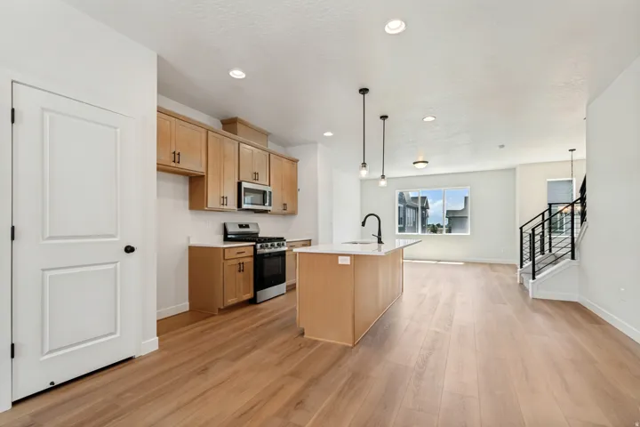 Open-concept kitchen featuring light-toned wood cabinetry, stainless steel appliances, and a central island with a sink and pendant lighting